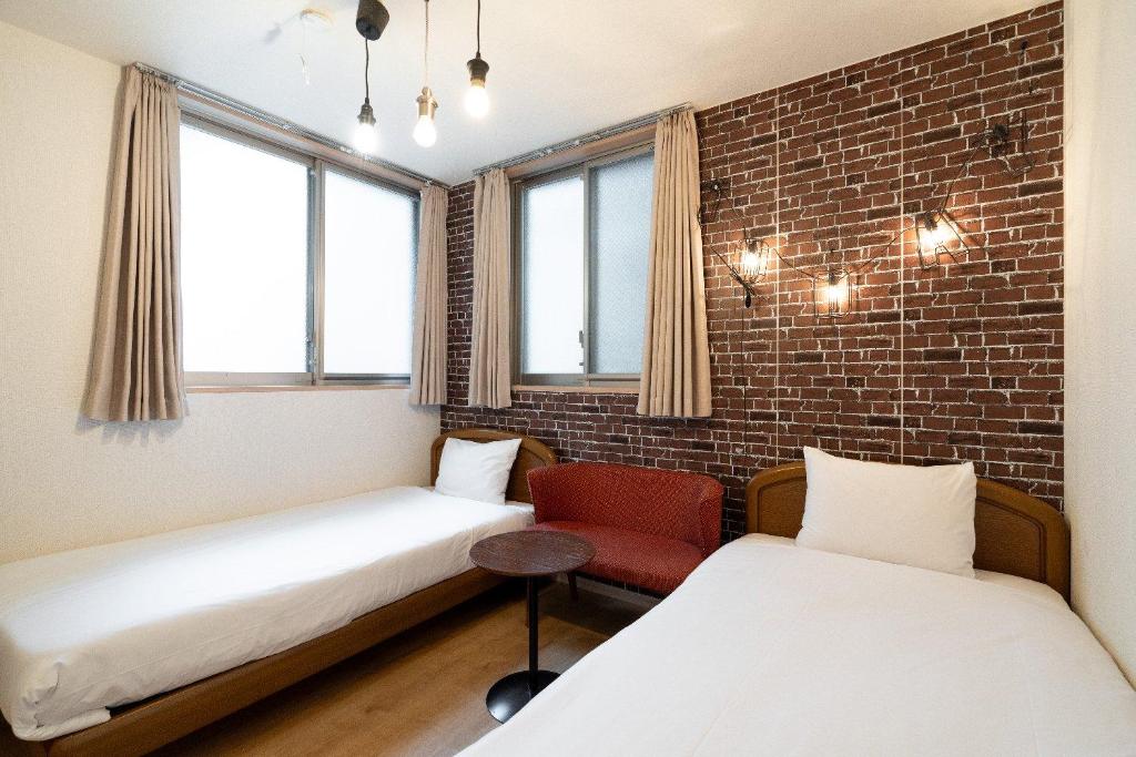 een kamer met 2 bedden en een rode stoel bij City Oasis in Tokyo