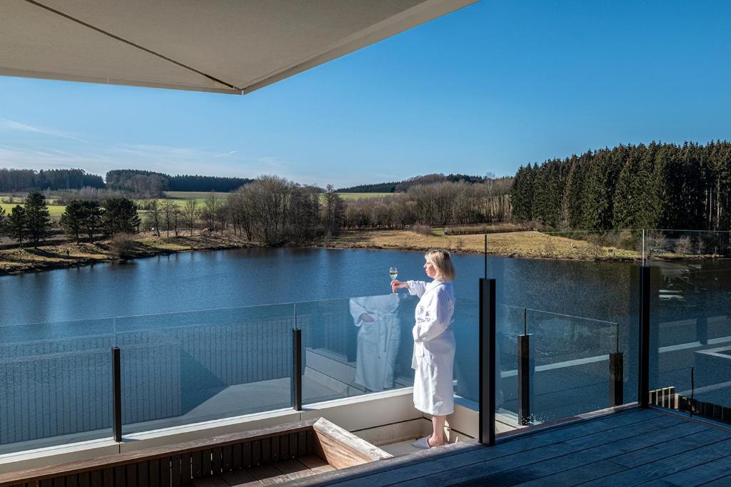 a woman standing on a balcony looking out at a lake at Anatura Luxembourg in Weiswampach
