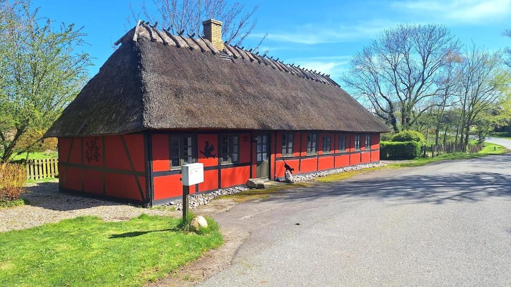 a red building with a thatched roof next to a road at Cozy holiday home in Dalby