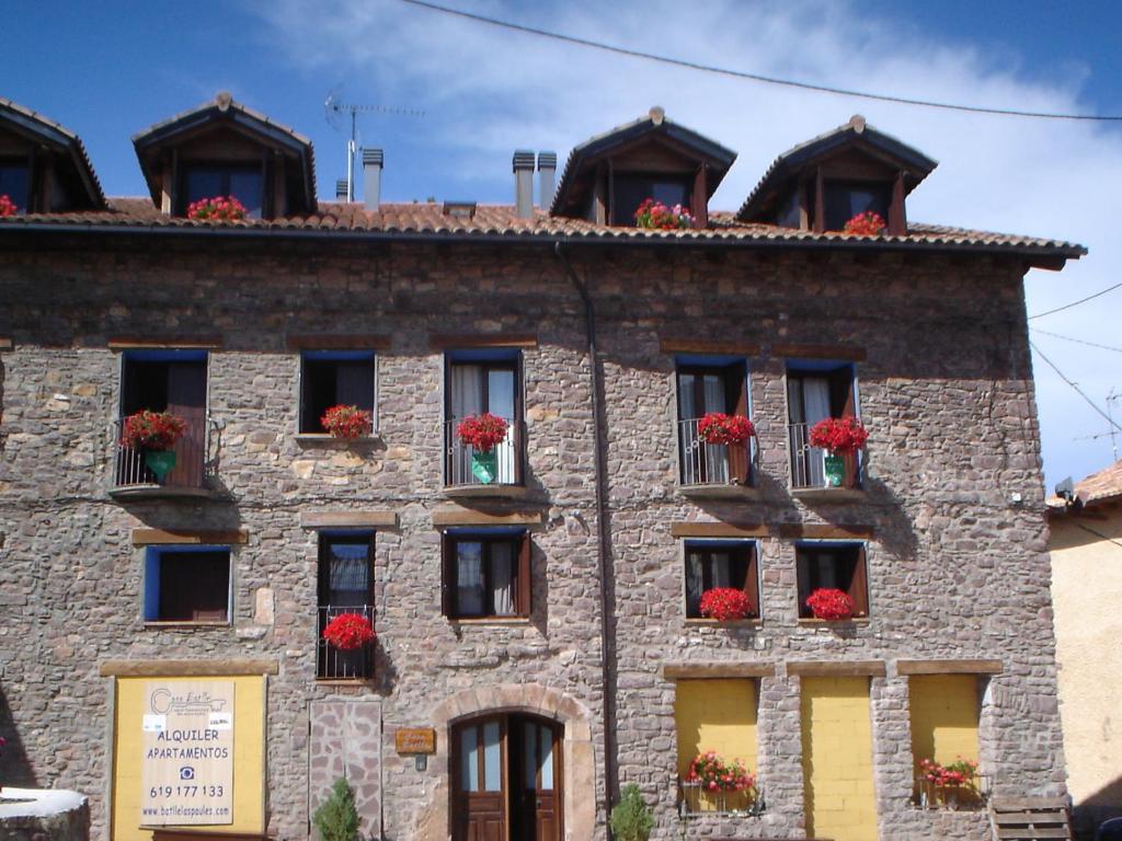 ein altes Steingebäude mit roten Blumen in den Fenstern in der Unterkunft Apartamentos Turísticos Batlle Laspaules in Laspaúles