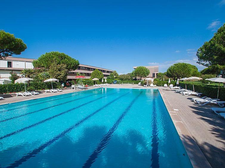 a large swimming pool with chairs and umbrellas at Appartamento in residence con piscina in Marina di Bibbona
