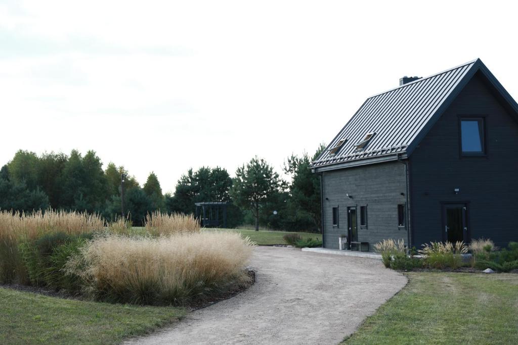 a black barn with a gravel driveway in front of it at Ežero Sapnas - Dream of the Lake in Lazdijai