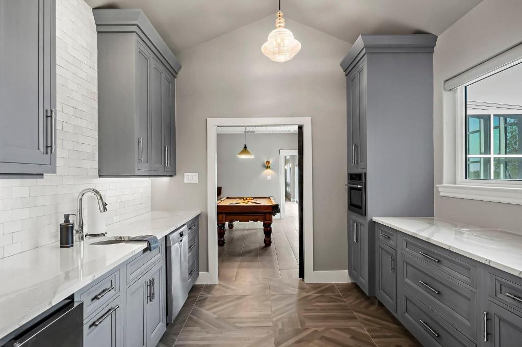 a kitchen with gray cabinets and a table in the background at Lazy River Ranch - Lazy River Pool, Golf & Pickleball in Kreutzberg