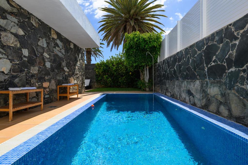 a swimming pool next to a house with a stone wall at Villa Viña del Mar in Maspalomas