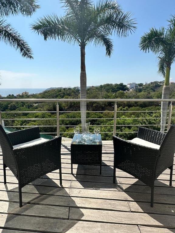 a patio with two chairs and a table and palm trees at Increíbles condominios con vista al mar in Tangolunda