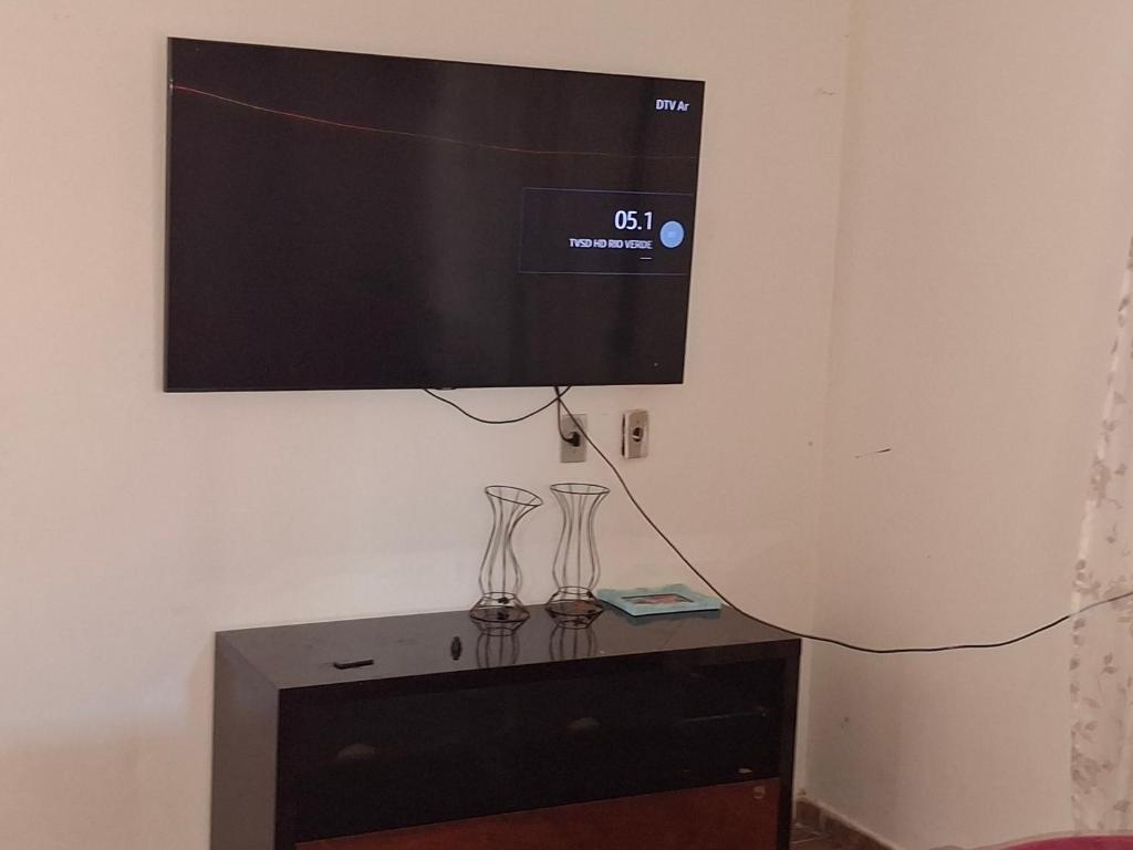 a flat screen tv hanging on a wall with two glasses at Casa Para TECNOSHOW Comigo Rio Verde GO in Rio Verde