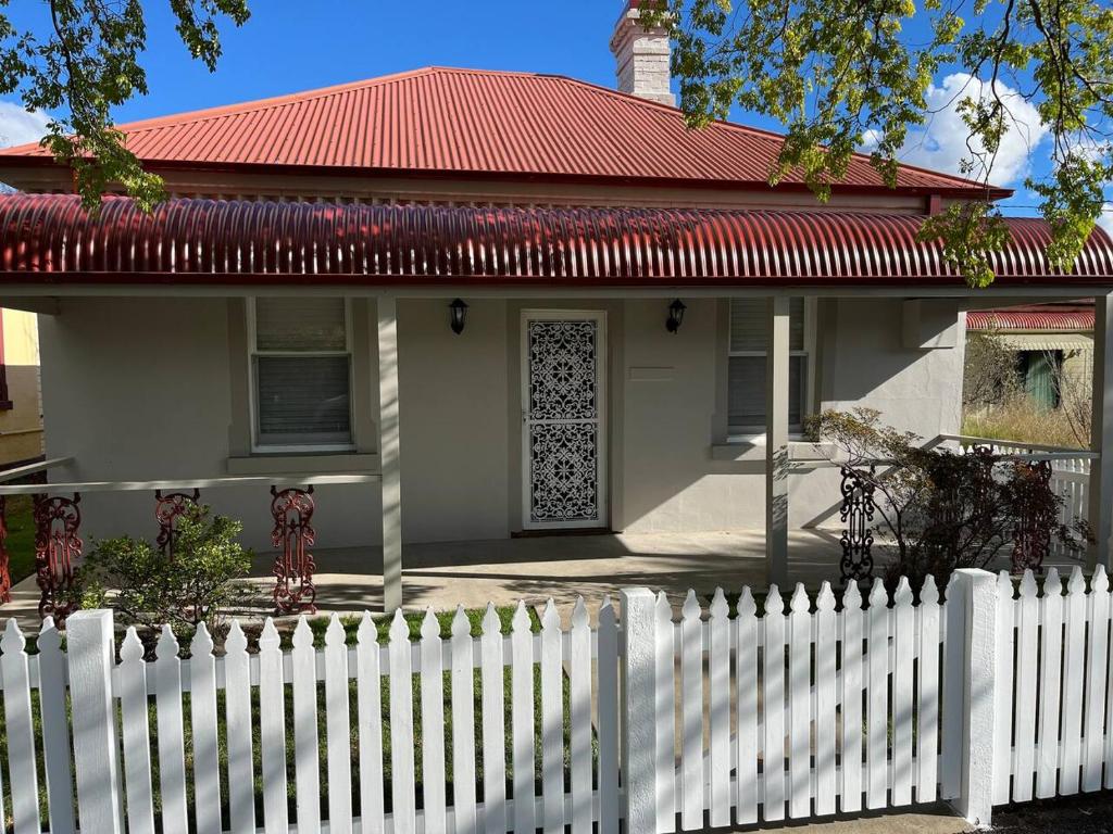 a white fence in front of a house with a red roof at Beautiful comfortable cottage in Orange