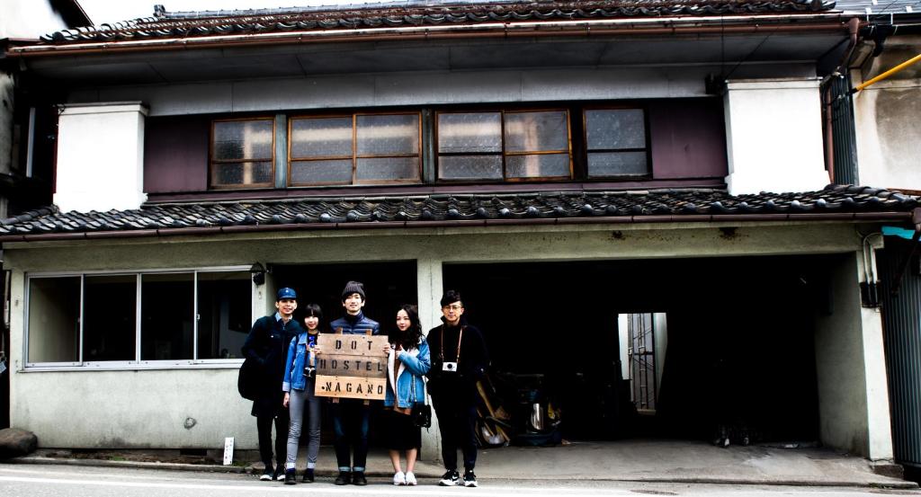 a group of people holding a sign in front of a building at Dot Hostel Nagano in Nagano