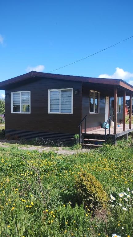 a black house with a porch and a field of flowers at Cabaña en condominio privada in Llanquihue