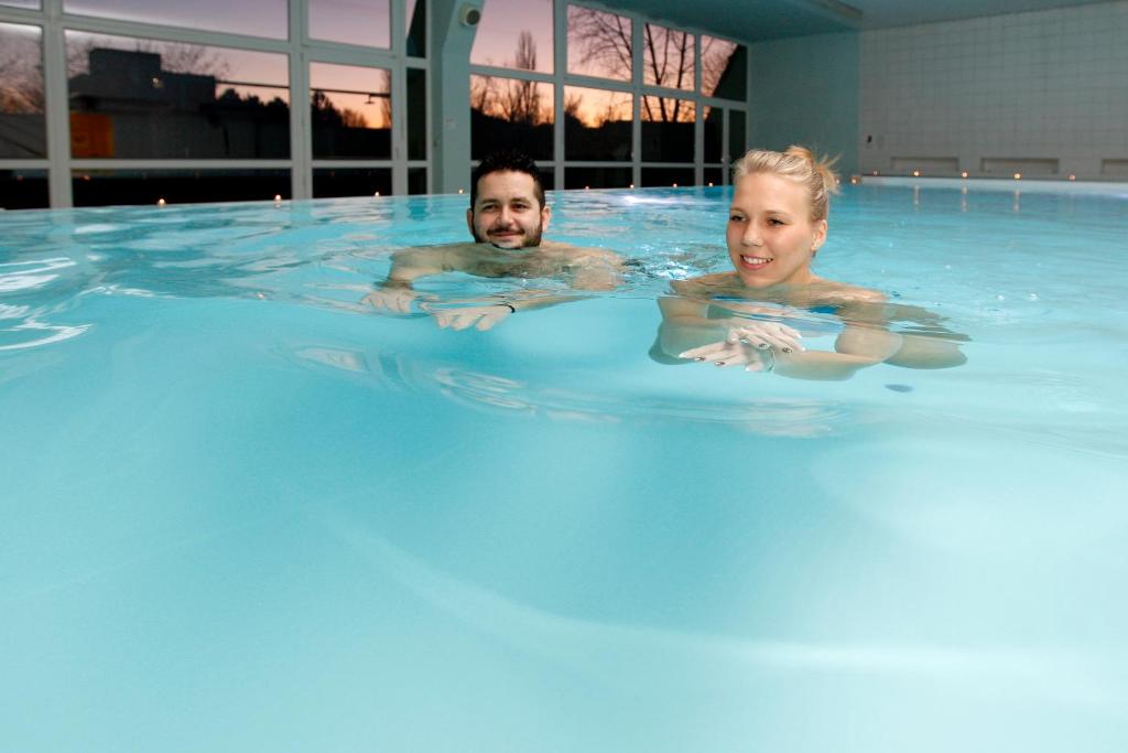 a man and woman swimming in a swimming pool at MÁJ Hotel Medical Wellness in Piešťany