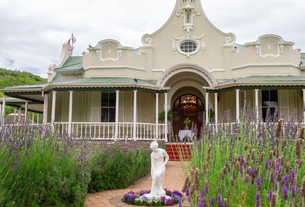 a statue in front of a house with purple flowers at Bakenskraal Ostrich Palace in Oudtshoorn