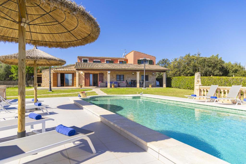 a pool with chairs and an umbrella and a house at Villa Las Comas de Dalt in Alcudia