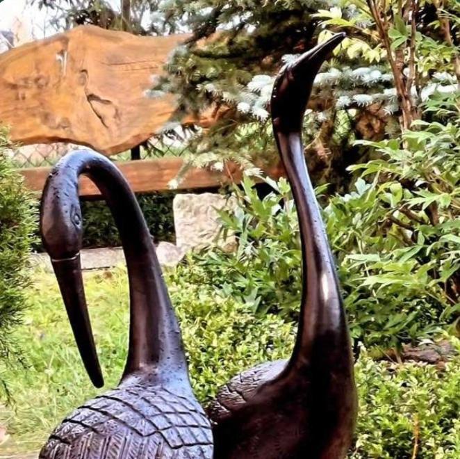 two black statues of birds standing next to a bench at Fajne Miejsce in Wambierzyce