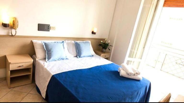 a bedroom with a bed with blue sheets and a window at Hotel Bruna in Cesenatico