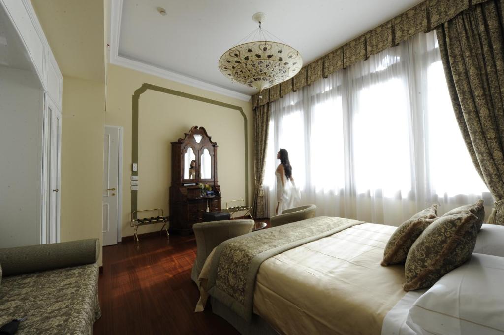 a bedroom with a bed and a woman standing in a window at Hotel Le Isole in Venice