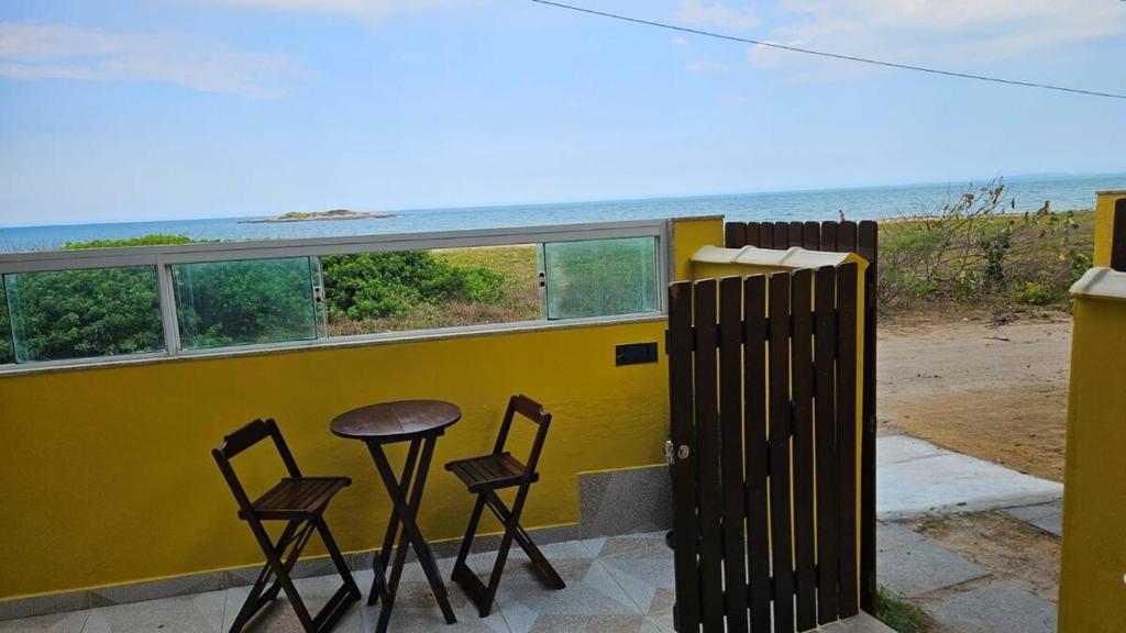 two chairs and a table in front of a yellow wall with the ocean at KITNET Beira Mar Prainha Barra - Rio das Ostra in Barra de São João