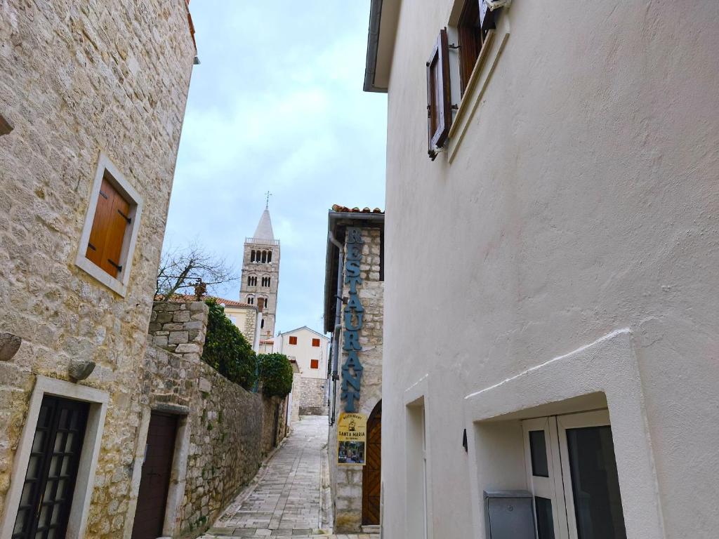 an alley between two buildings with a clock tower in the background at House Nonina kuca in Rab