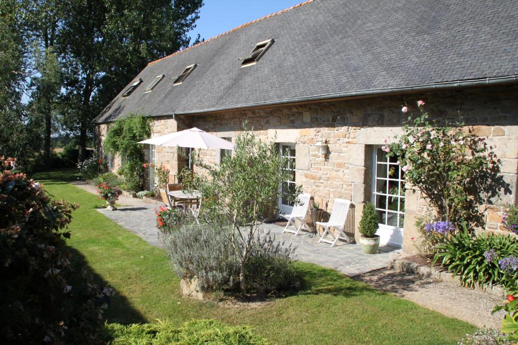 Ce cottage en pierre comprend une table, des chaises et un parasol. dans l'établissement Résidence CoatArmor, à Tonquédec