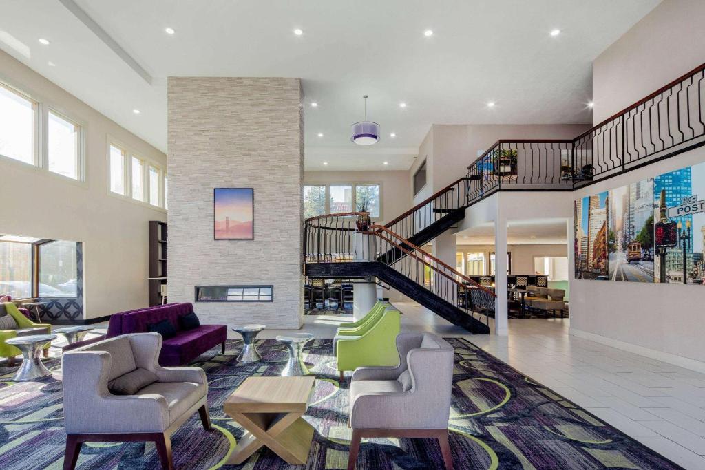 a lobby with a staircase and chairs and tables at La Quinta by Wyndham Oakland - Hayward in Hayward