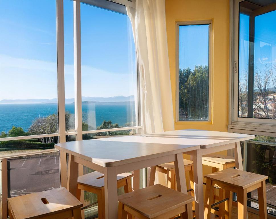 - une table et des chaises dans une pièce dotée de grandes fenêtres dans l'établissement T3 avec vue mer imprenable dans une résidence avec piscine, à Six-Fours-les-Plages