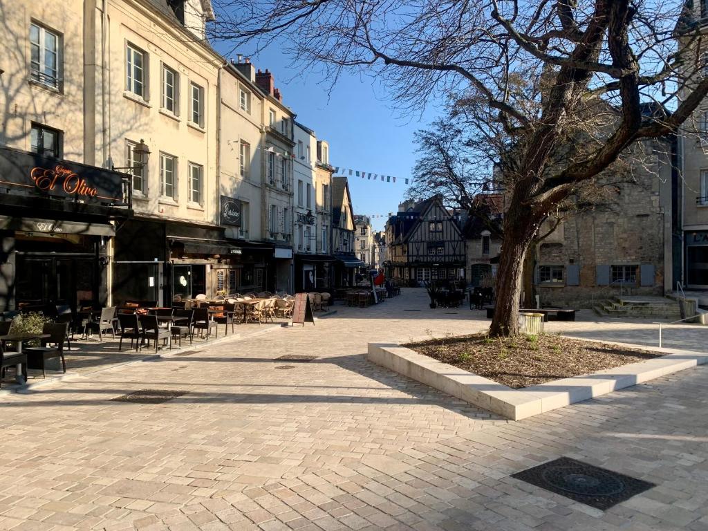 une rue de la ville avec un arbre, des tables et des chaises dans l'établissement Le Nid Du Vaugueux, à Caen