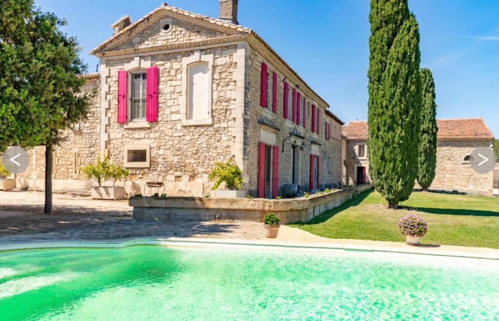 une vieille maison en pierre avec des fenêtres rouges et une piscine dans l'établissement Bâtisse au cœur d'un vignoble, à Montfrin