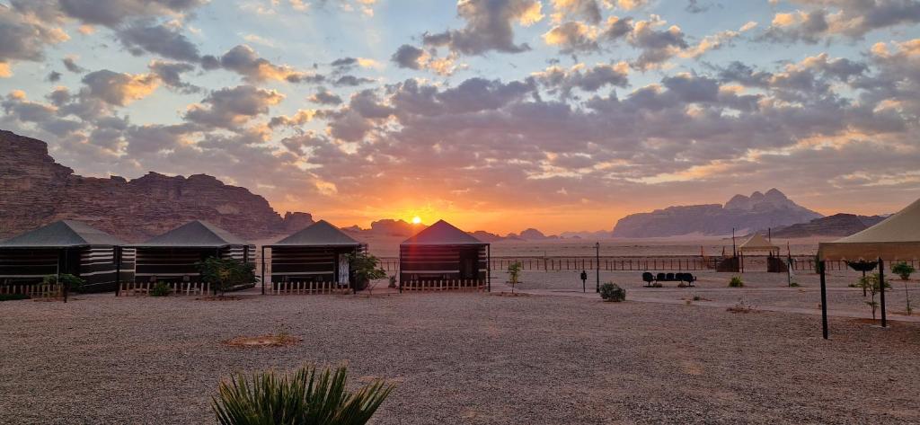 a sunset over a desert with a group of buildings at Dream Bedouin Life Camp Wadi Rum in Disah