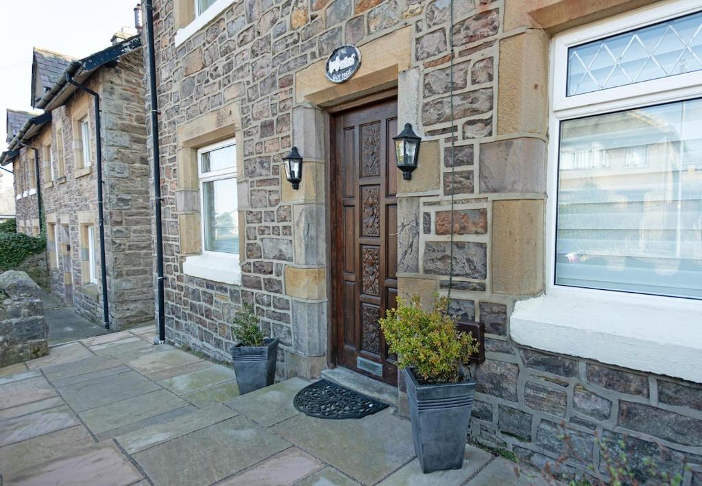 a brick building with a wooden door and two potted plants at Smithy Cottage in Heysham