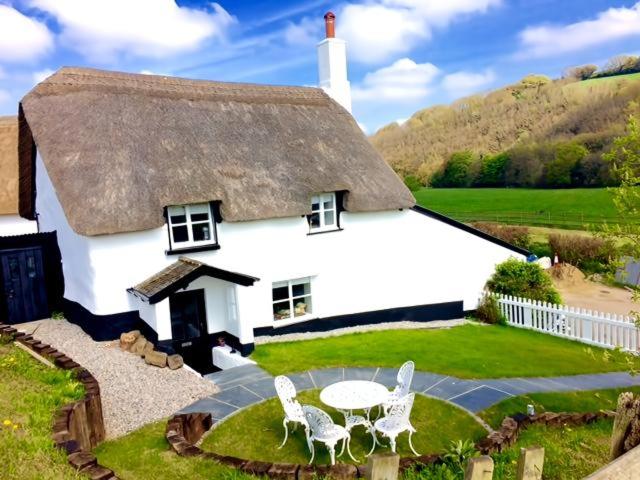 a large white house with a table and chairs at Cosy and unique Thatched Cottage on Dartmoor in Bridford