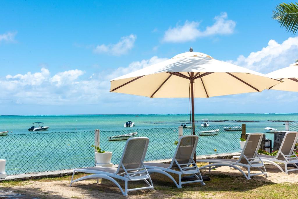 a group of chairs and an umbrella on a beach at Quaint 2BDR beach apartment in a fishing village in Grand Gaube