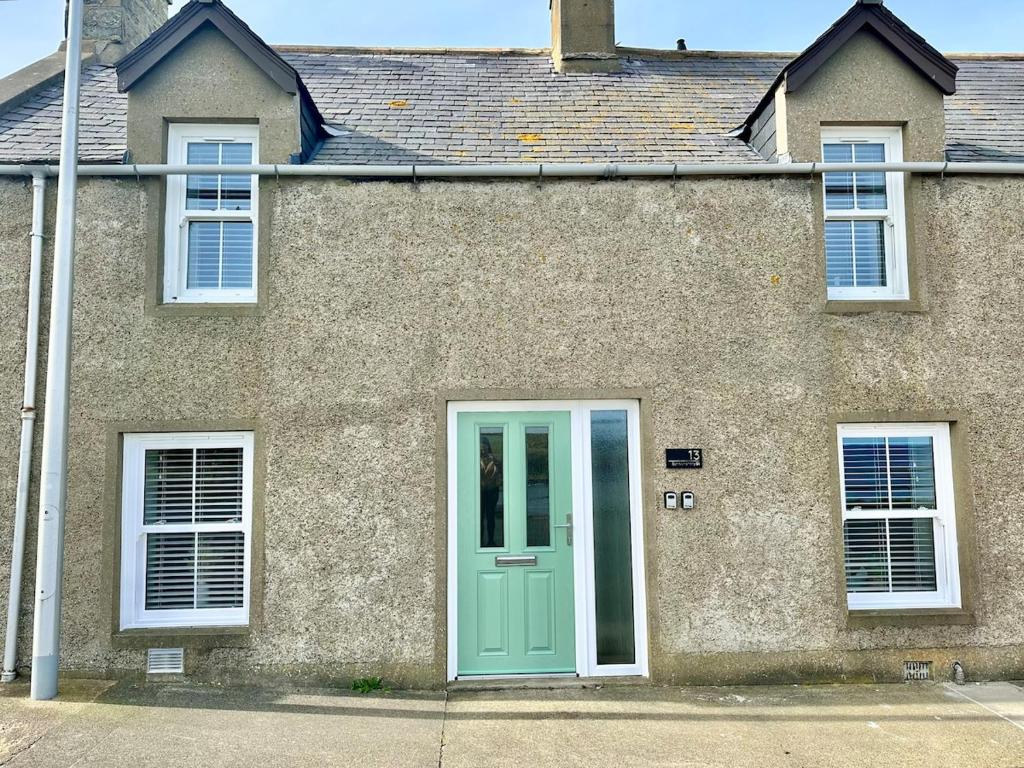 a house with a green door and two windows at Luxury Coastal Cottage in Portsoy