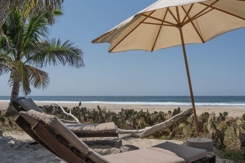 een stoel en een parasol op het strand bij Cabanas Adobe Frente Al Mar in Puerto Escondido
