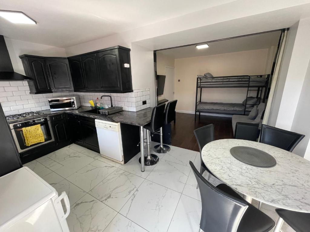 a kitchen with black cabinets and a table with chairs at Garden Apartment nr Heathrow Airport & Elizabeth Line Train Station with Parking for 2 cars in Hayes