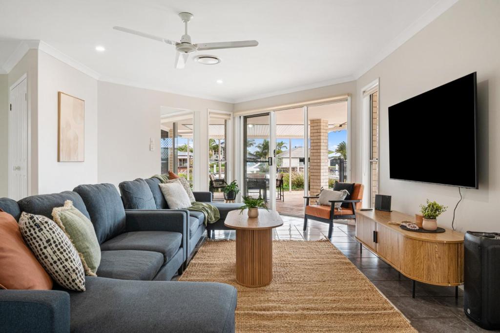 a living room with a blue couch and a tv at Topsail Tides Absolute Canal Waterfront Banksia Beach in Banksia Beach