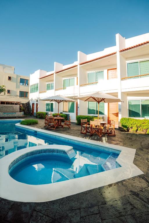 a pool in front of a building with tables and umbrellas at Hotel Ninfa in Puerto Ayora