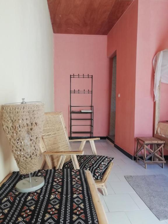 a room with a bed and a chair and pink walls at Maison Manour chambre 'soft breeze' in Mbour