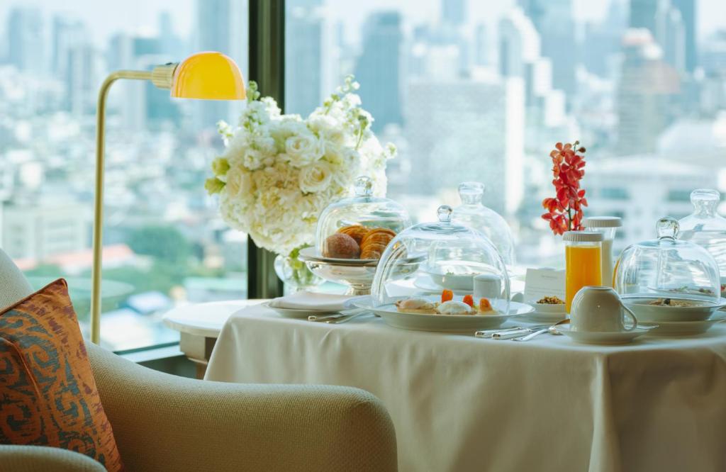 a table with a plate of food and a vase of flowers at The Peninsula Bangkok in Bangkok