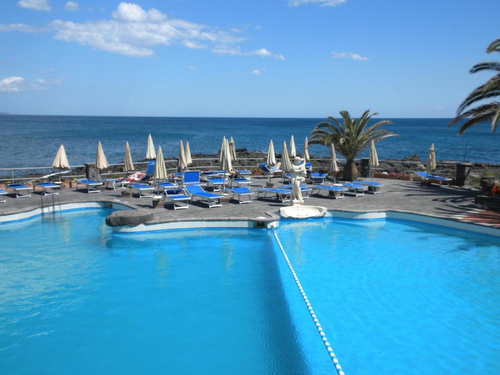 una piscina con sillas y el océano en el fondo en Arathena Rocks Hotel, en Giardini Naxos
