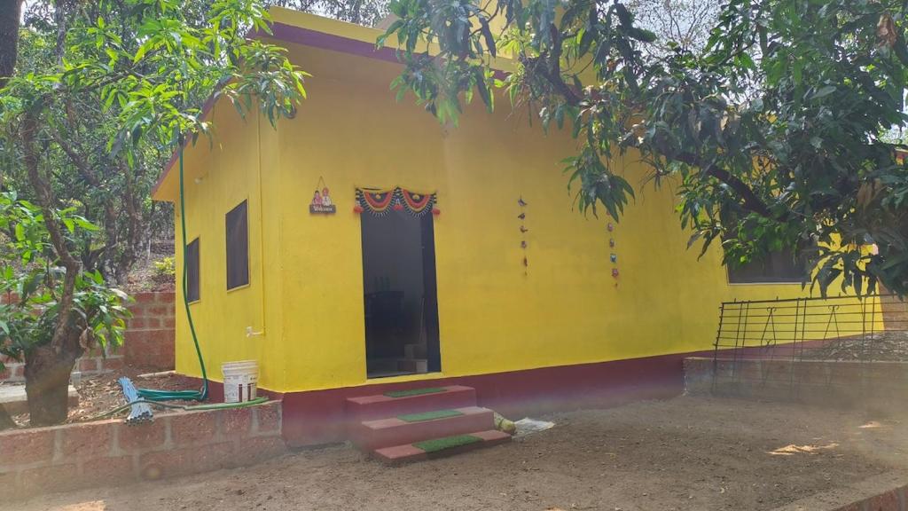 a yellow house with a door and a tree at Rukhmini Niwas in Pural