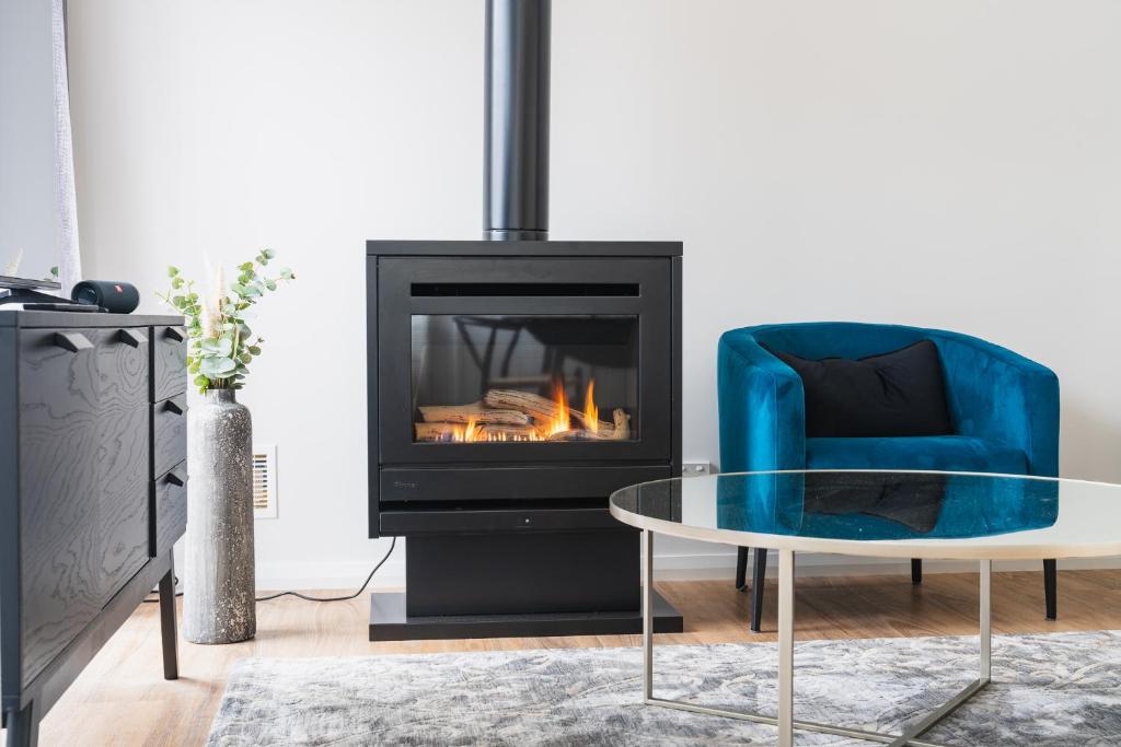 a living room with a fireplace and a blue chair at Wine Tree Estate Chalets in Denmark