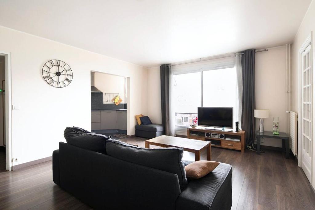 un salon avec un canapé noir et une télévision dans l'établissement Emile Zola Asnière - KP -Spacious apt for 6 with porch Asnière sur Seine, à Asnières-sur-Seine
