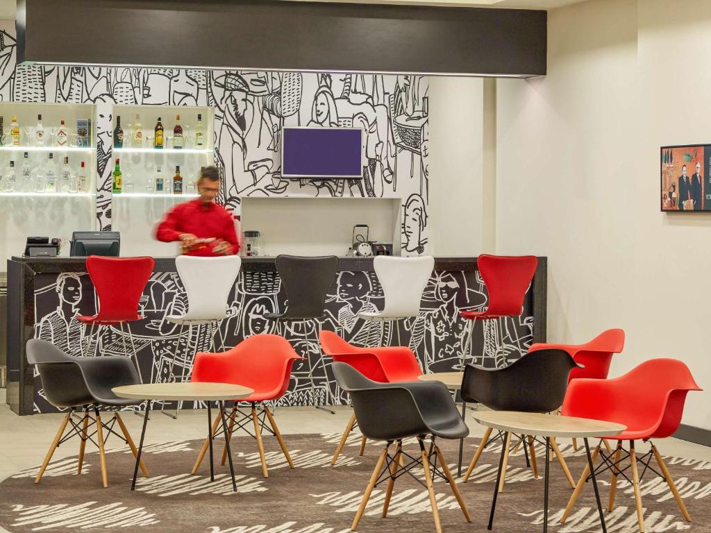 a bar with red chairs and a woman in the background at ibis Ankara Airport Hotel in Ankara