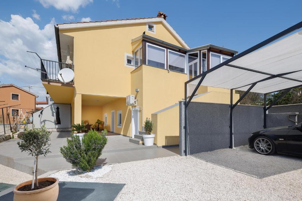 a yellow house with a black car parked in the driveway at Apartment Miha in Loborika