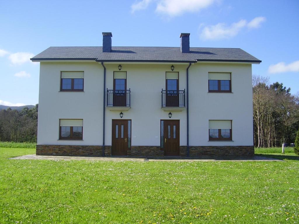 Casa blanca con puertas marrones y un campo verde en Apartamentos Turísticos La Senra, en Castropol