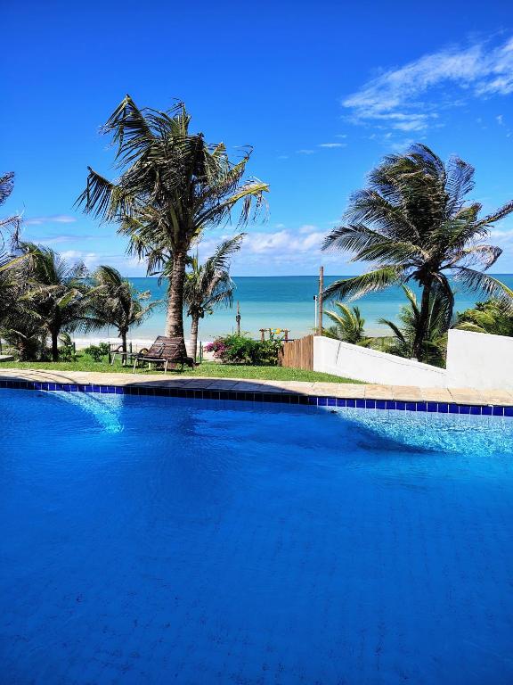 a large blue swimming pool with palm trees and the ocean at CosteiraPRAIASOLPontaNegra, Natal-RN in Natal