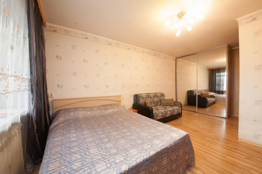 a bedroom with a bed and a chair and a mirror at Kvartirov Apartments at Kosmos in Krasnoyarsk