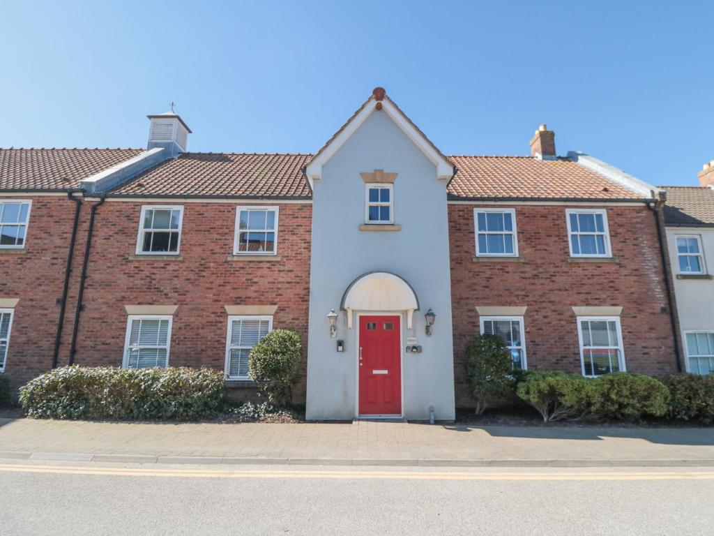 a brick house with a red door on a street at Sunny Bay in Reighton