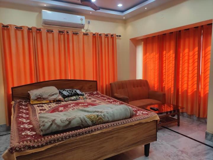 a bedroom with a bed and a chair and orange curtains at Luxury penthouse on budget in Kolkata