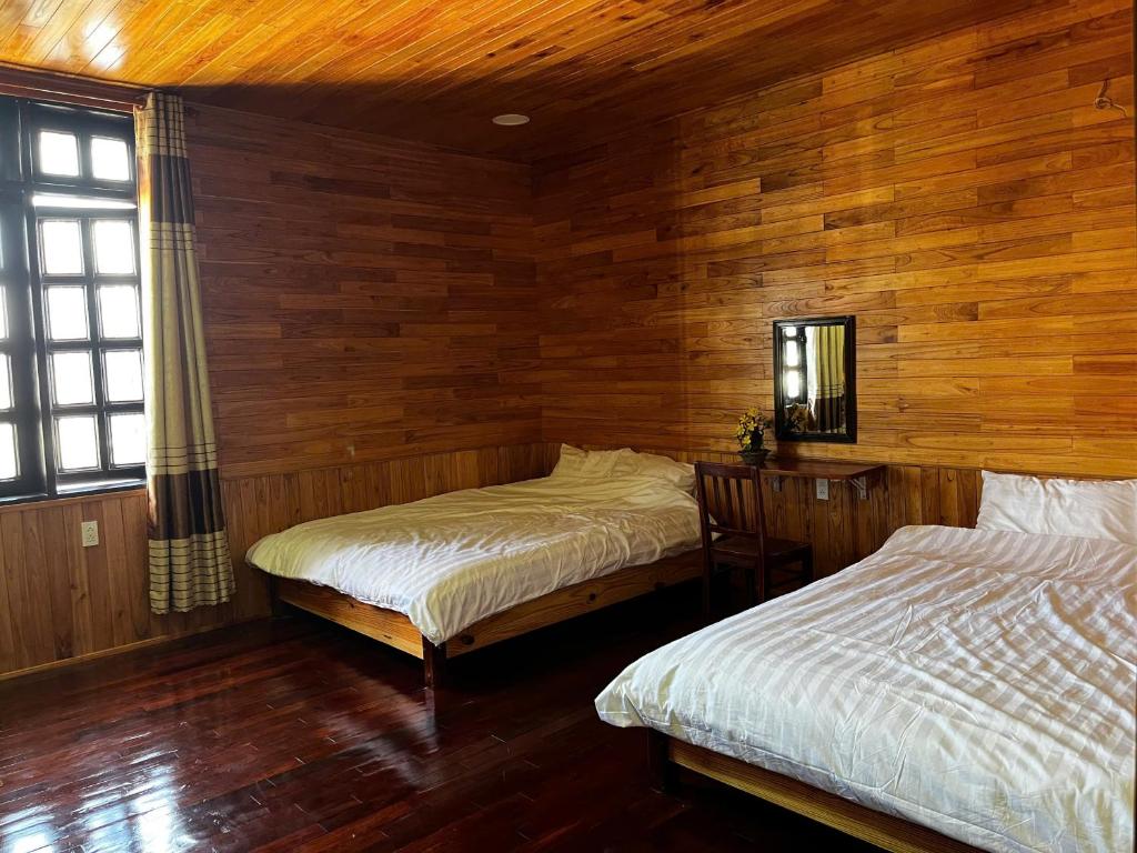 two beds in a room with wooden walls at Homestay Nhà Mộc in Da Lat