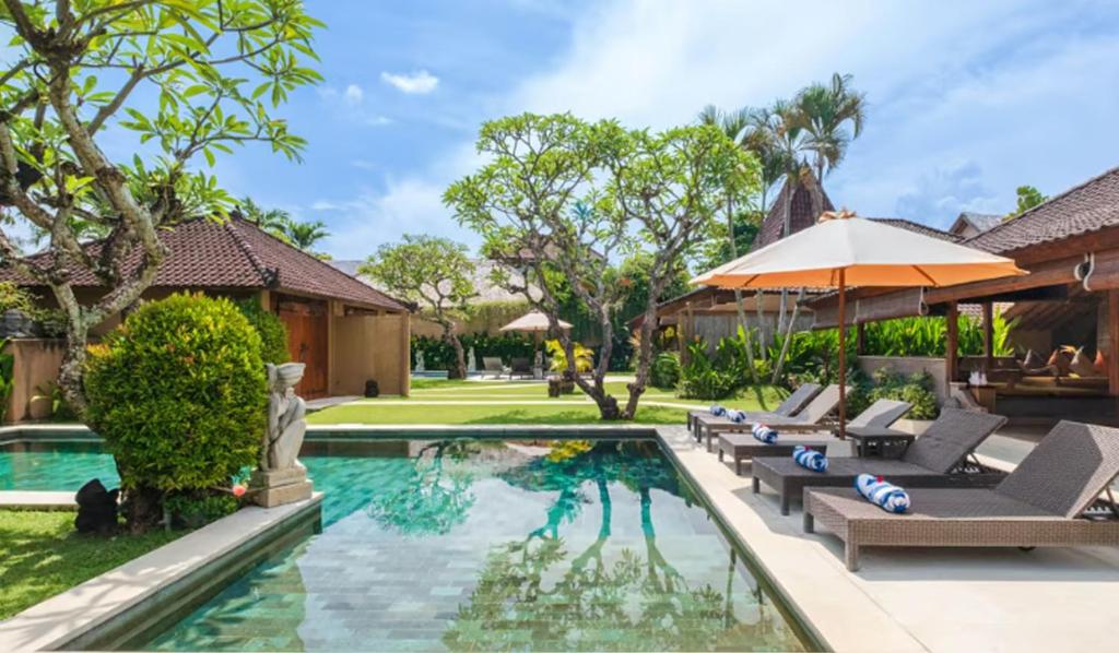 a pool with lounge chairs and an umbrella next to a house at Bali Dyana Villas in Seminyak